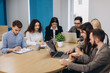 © JJ Studio - Multi ethnic people entrepreneur, small business concept. Woman showing coworkers something on laptop computer as they gather around a conference table.