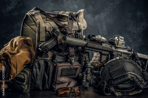 Military uniform and equipment. Body armor, gun, assault rifle, helmet, night vision goggles. Studio photo against a dark textured wall