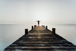 Person steht mit offenen Armen bei Sonnenuntergang auf einem Steg am Meer und genießt die Freiheit