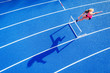 Top view of female runner crossing hurdle on tartan track