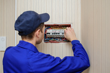 Wall Mural - back view of a young eletrician in blue overall disassembling a electrical panel with fuses in a house.