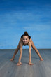 © Eno1 - Girl gymnast smiles and shows a gymnastic exercise on the floor on a blue background. The girl is smiling and fooling around.