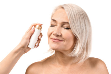 Wall Mural - Female hand applying serum onto mature woman's face against white background