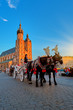 Sunset in Krakow, Polland. Two Horses In Old-fashioned Coach At Old Town Square in beautiful sunset light with St. Mary's Basilica Famous Landmark On Background