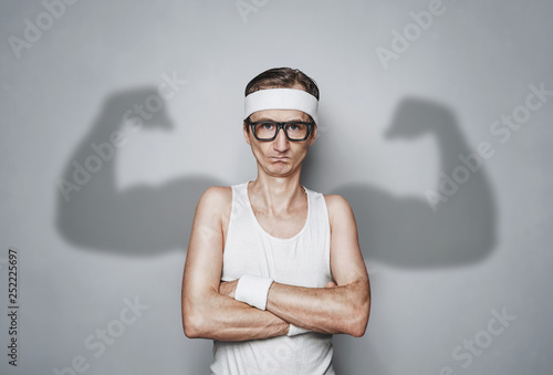 Cuadros en Lienzo Funny sport nerd with shadow muscle arms over gray wall with copy space