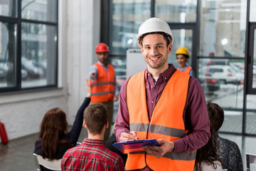 Selective focus of happy fireman holding clipboard near coworker giving talk on briefing