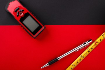 Tape measure, laser distance meter and pencil on matte black and red background