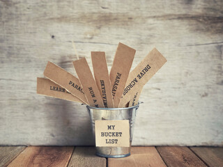 Motivational and inspirational concept - My Bucket List written on paper. There are list of wishes written on papers and placed inside the bucket. Blurred vintage styled background.