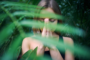 Portrait of cute young woman meditating and doing namaste hand in jungle. Sunny day