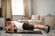© estradaanton - Young well-built man go in for sports in apartment. He stand in plank position on carimate. Guy look forward. He doing workout alone.