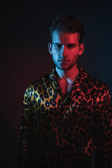 Wall Mural - Art neon glamor fashion men's model tests. Handsome guy model posing in leopard shirt on a blue and red filter. Fashion photography in the studio.