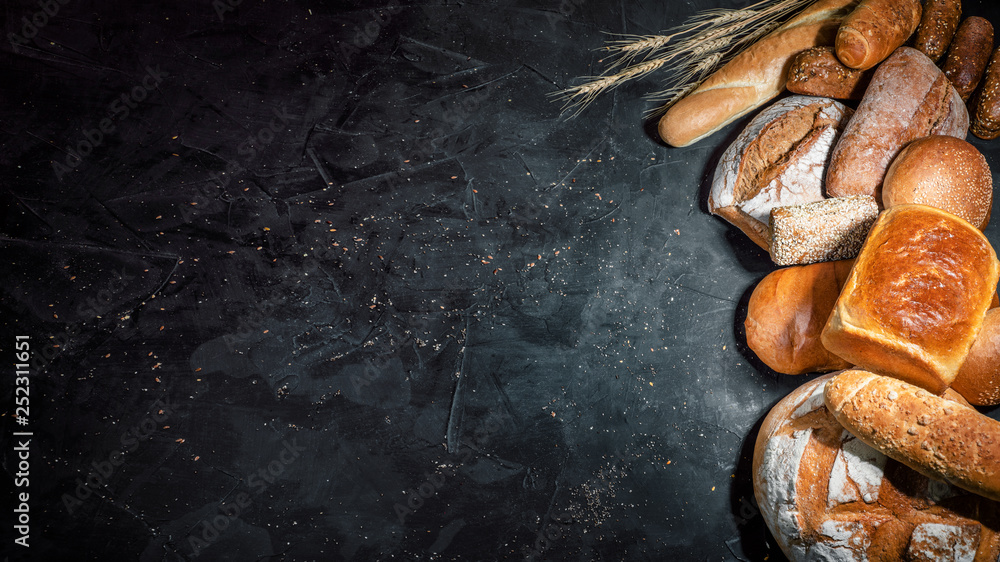 Assortment of fresh baked bread on dark background. White and rye bread, buns with copy place - obrazy, fototapety, plakaty 
