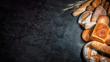 Fototapeta Tulipany - Assortment of fresh baked bread on dark background. White and rye bread, buns with copy place