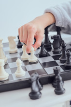 Crop Hand Of Child Holding Figure On Chess Board On Grey Background 