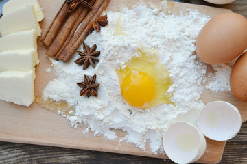 White flour with eggs, butter, cinnamon sticks, spicy anise stars and wooden spoon on a cooking board