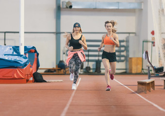 Two young athletic women running in sports arena indoors