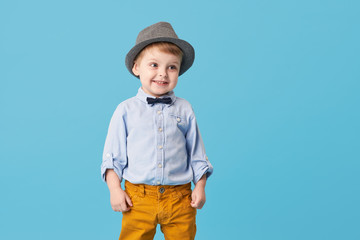 Wall Mural - Portrait of happy joyful  little boy isolated on blue background. Toddler child in hat and fashionable suit smiling and have a fun. Copy space for text right side