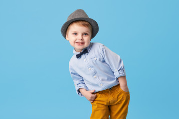 Portrait of happy joyful  little boy isolated on blue background. Toddler child in hat and fashionable suit smiling and have a fun 