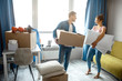 © estradaanton - Young family couple bought or rented their first small apartment. They stand in room with box and pillows. People look at each other.