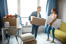 Young Family Couple Bought Or Rented Their First Small Apartment. They Stand In Room With Box And Pillows. People Look At Each Other.