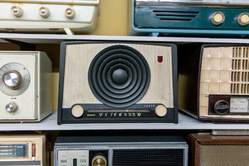 Retro broadcast radio receivers on wooden shelf against yellow background.