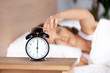 © fizkes - Young woman lying in bed, woken by alarm signal, turning off clock