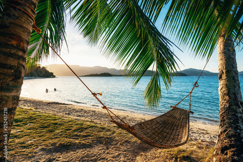 Empty hammock between two palm trees on the beach at sunset Poster Mural XXL