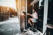 © skyNext - A wide-angle shot with a copy space area on the left for your ad message: African-American woman is interracting with her cellphone while sitting in a street bar with a laptop and a glass of juice