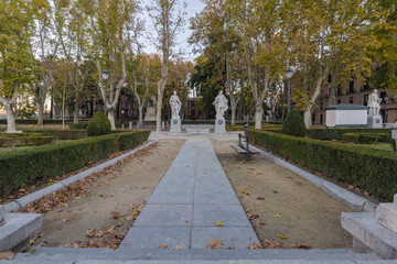 Looking down a sidewalk in a beautiful park with two statues on a clear day