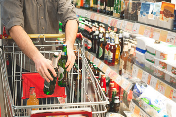 Man holds two bottles of beer in his hands and puts them in a cart for shopping.Buyer buys a beer in a supermarket, hands with bottles close up. Buying in a supermarket puts the goods in the basket.