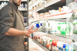 Man in a shirt with two bottles of yogurt in his hands. Buyer is buying a dairy product in a supermarket. Hands of a man with milk close up, background of a light refrigerator with shelves. Copyspace