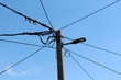 Concrete electrical utility pole with modern LED public light and multiple electrical wires going in all directions on clear blue sky background