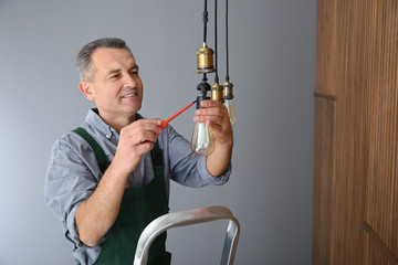 Wall Mural - Electrician with screwdriver repairing ceiling lamp indoors. Space for text