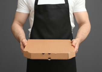 Canvas Print - Waiter in apron with pizza box on grey background, closeup. Food delivery service