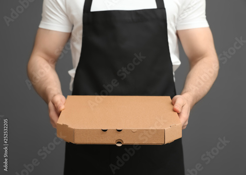 Fotomural Waiter in apron with pizza box on grey background, closeup