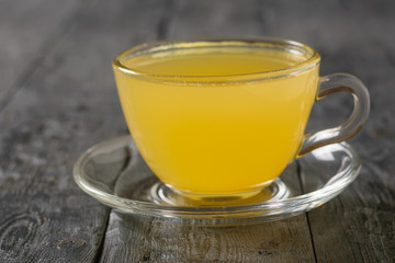 Glass bowl with saucer with ginger root drink and citrus on black table.