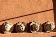 Straw Beach Hats Standing On Terracotta  Clay Wall.  Bright Sunlight And Hard Shadows.