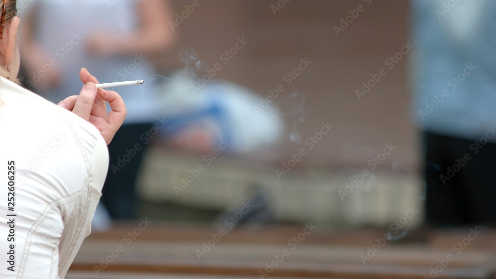 Female hand holding burning cigarette. Woman smoking cigarette outdoors, back view. Harmful habit concept. - obrazy, fototapety, plakaty 