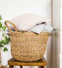 Wicker Basket With Gray Cushions On A Wooden Vintage Chair Against A White Wall