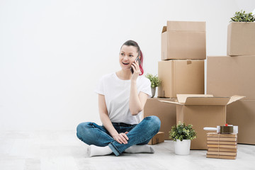 Wall Mural - Young beautiful girl with colored hair in a white T-shirt and jeans, talking on the phone and writes messages against the background of cardboard boxes and things.