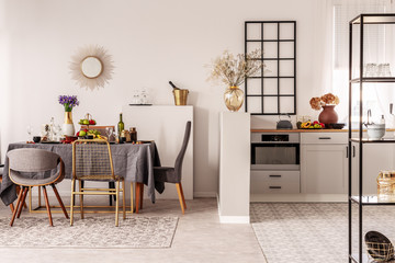 Wall Mural - Stylish open plan kitchen and dining room interior with white cupboard and long table with grey tablecloth and food