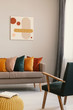 © Photographee.eu - Abstract painting on grey wall of retro living room interior with beige sofa with pillows, vintage dark green armchair and yellow pouf with book
