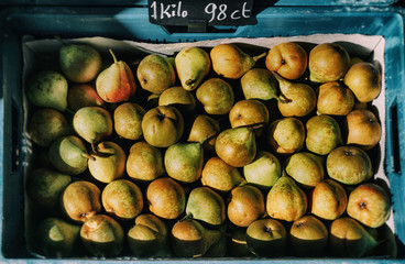 Ripe windfall pears for sale per kilo at farmers market in blue crate. Fall colors in bright sunlight. 