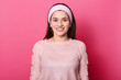 Image of european lovely woman with dark hair, wears rose sweater. Lady being in good mood while posing alone in studio. Young model with hairband. Smiling girl isolated over pink background.