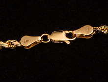 Clasp On A 14k Gold Necklace With Markings On A Black Background