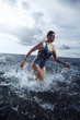 Young woman in swimsuit running in the water during triathlon competition