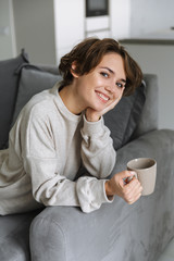 Wall Mural - Happy young woman sitting on a couch at home