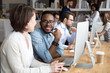 © fizkes - African male caucasian female talking sitting at desk near pc