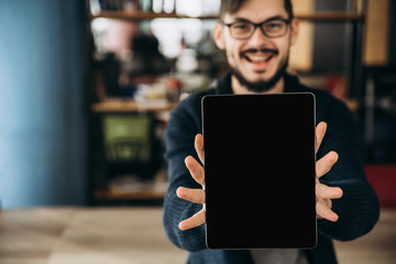 Wall Mural - Copy space. Space for text. Empty screen. Modern smiling guy in glasses is holding a tablet with a blank screen. Close-up