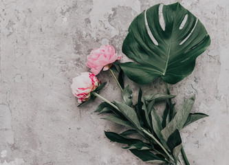 Poster - Flat lay pink peonies on stone background with monstera leaf. Creative floral image. Happy mother's day. International women day. Greeting card mockup